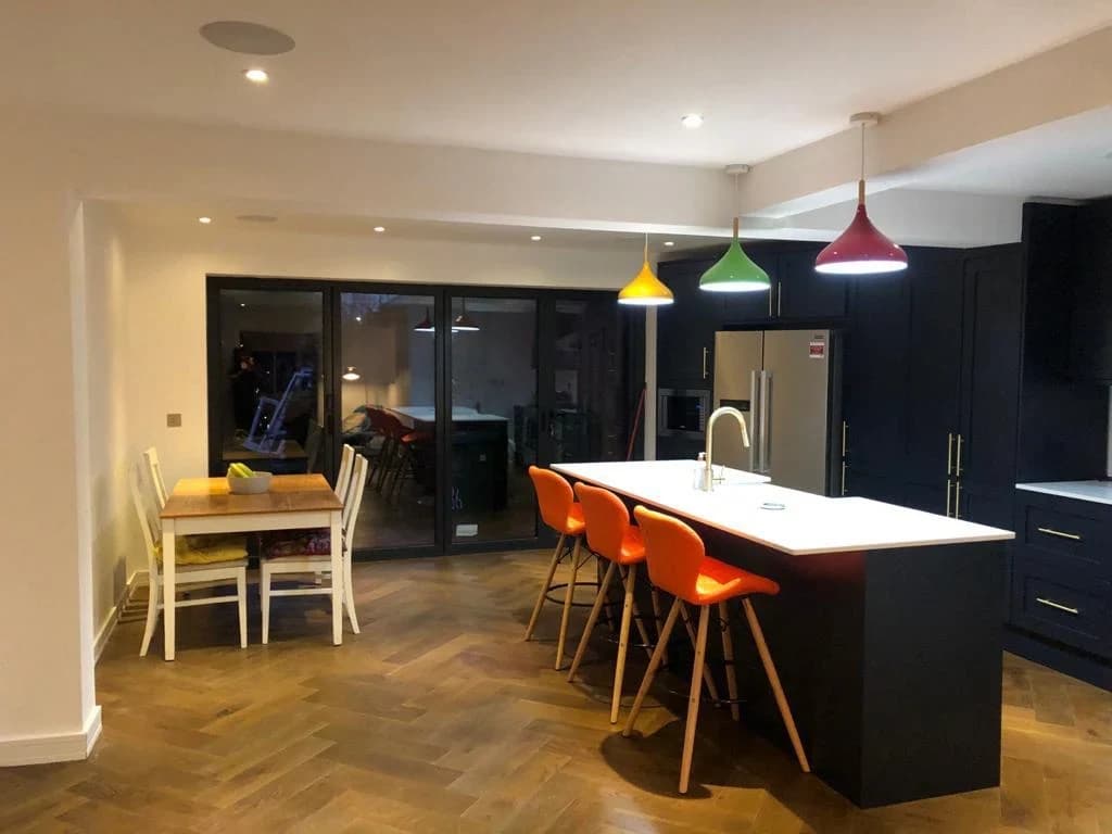 Open-plan kitchen with dark cabinets and statement orange chairs
